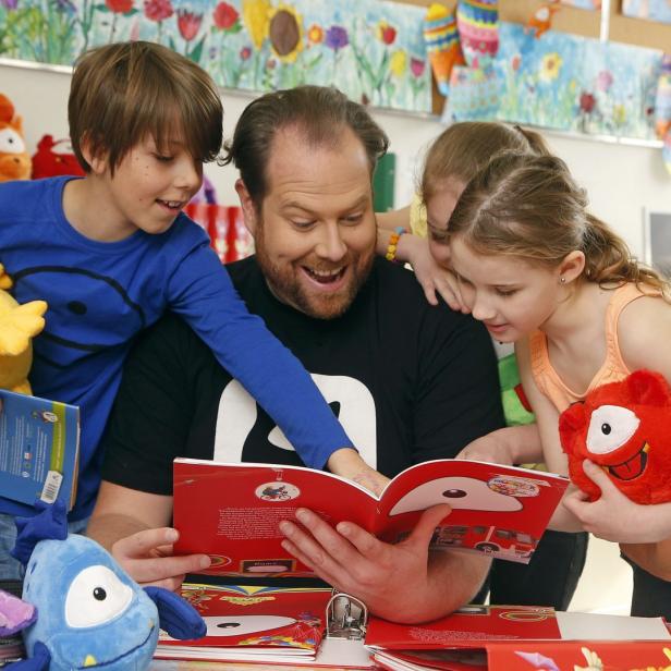 Ein Mann liest mit drei Kindern in einem Buch mit bunten Illustrationen.