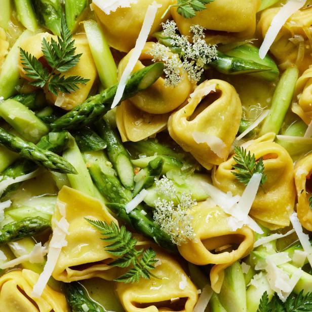 Eine Nahaufnahme von Tortelloni mit Spargel, Käse und kleinen weißen Blüten.