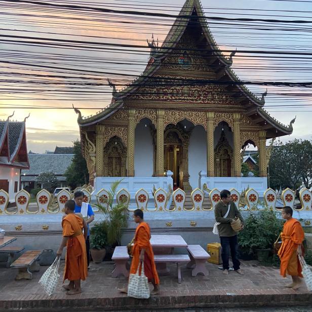 Mehrere buddhistische Mönche in orangefarbenen Roben vor einem verzierten Tempelgebäude.