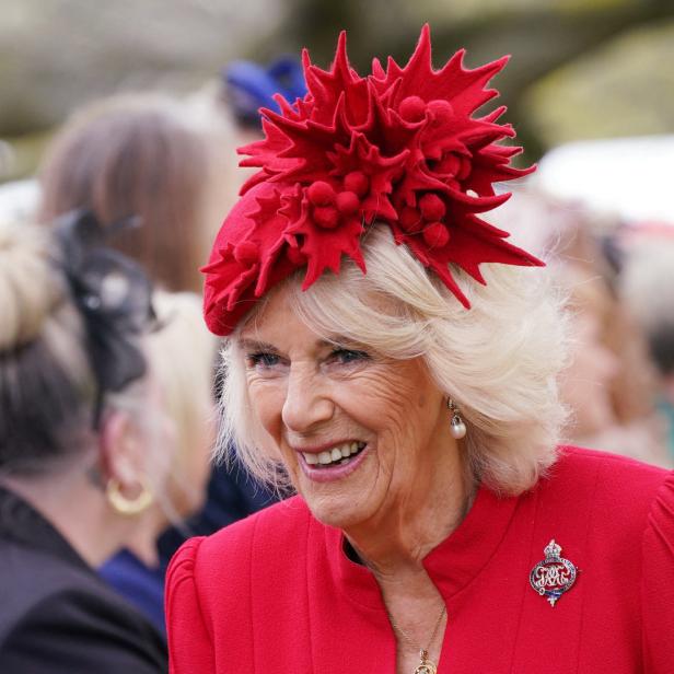 Königin Camilla lächelt in einem roten Kleid und mit einem roten Hut.