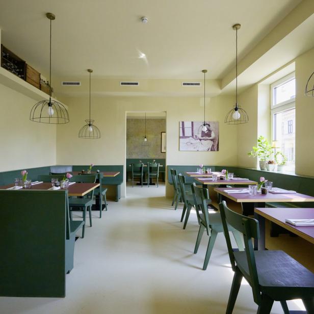 Ein Restaurant mit grünen Sitzecken und Tischen mit rosa Tischplatten.
