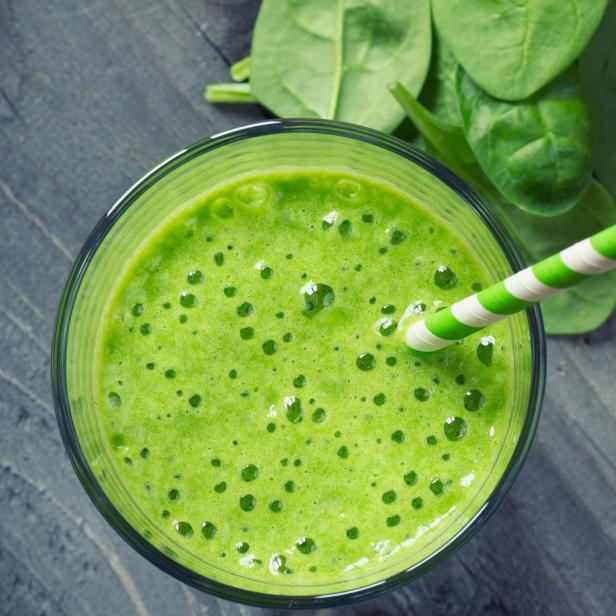 Ein grüner Smoothie mit einem Papierstrohhalm und frischem Spinat auf einem Holztisch.