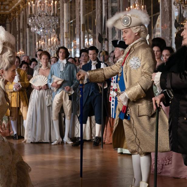 Szene in einem opulenten Ballsaal mit kostümierten Personen im Stil des 18. Jahrhunderts.