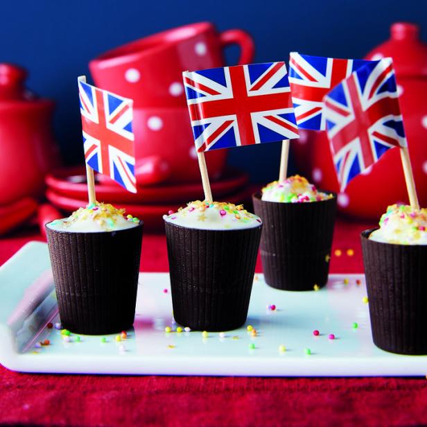 Vier Cupcakes mit britischen Flaggen und bunten Streuseln stehen auf einem Tisch.