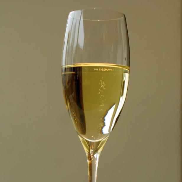 Ein Glas mit einem hellen, sprudelnden Getränk steht auf einem Tisch.