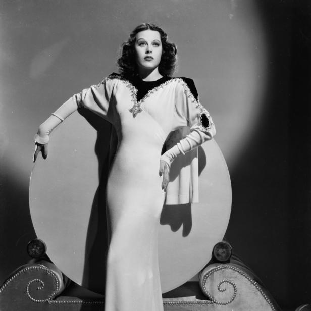 Hedy Lamarr posiert in einem langen, hellen Kleid vor einem runden Hintergrund.