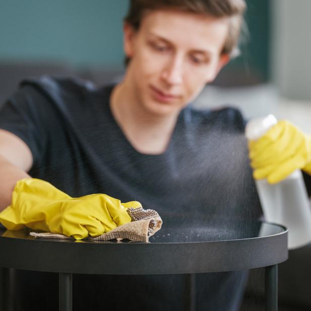 Ein Mann putzt mit gelben Handschuhen und einem Lappen einen schwarzen Tisch.