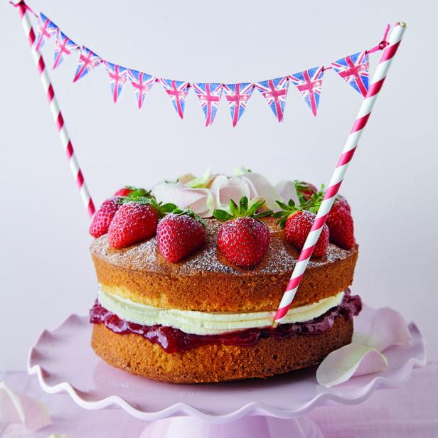 Ein Victoria Sponge Cake mit Erdbeeren und britischer Flaggen-Girlande auf einem rosa Teller.