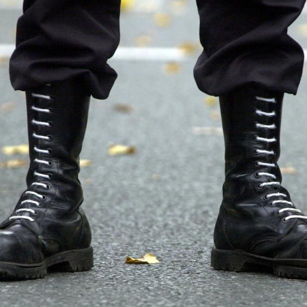Zwei schwarze, hohe Schnürstiefel stehen auf einer Straße mit einigen gelben Blättern.