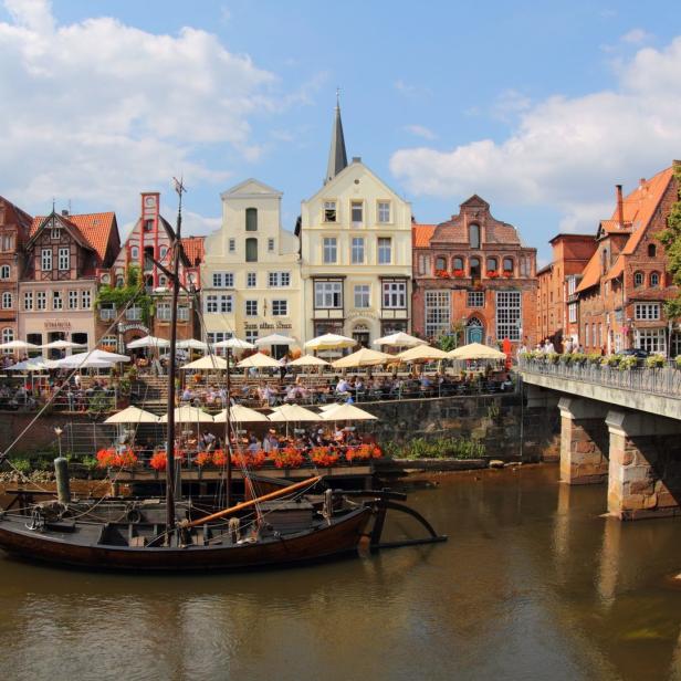 Ein historisches Segelboot auf der Trave in Lübeck vor einer Reihe von Restaurants am Ufer.
