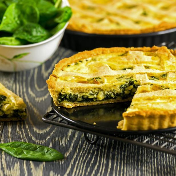 Eine angeschnittene Quiche mit Spinatfüllung auf einem dunklen Tisch.