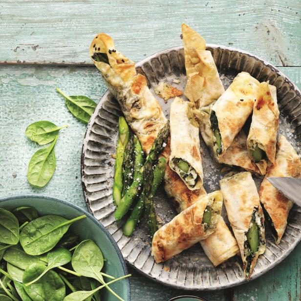 Eine Platte mit Filoteigröllchen, gefüllt mit Spargel und Spinat, dazu eine Schale mit frischem Spinat.