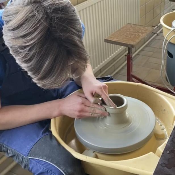 Eine Person formt mit den Händen Ton auf einer Töpferscheibe.