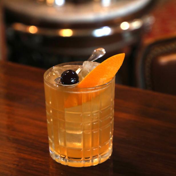 Ein Cocktail mit Eis, einer Orangenscheibe und einer Kirsche auf einem Holztisch.