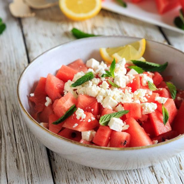 Ein Schüssel Wassermelone mit Feta und Minze auf einem Holztisch.