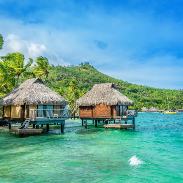 Zwei strohgedeckte Bungalows stehen auf Stelzen im türkisfarbenen Wasser.