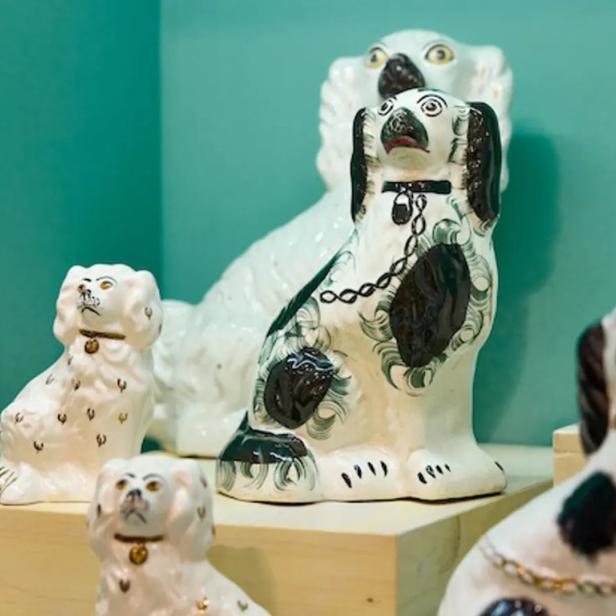 Mehrere bemalte Porzellanhundfiguren stehen auf einem Regal.