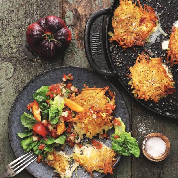 Rösti mit Salat und einer dunklen Tomate auf einem rustikalen Holztisch.