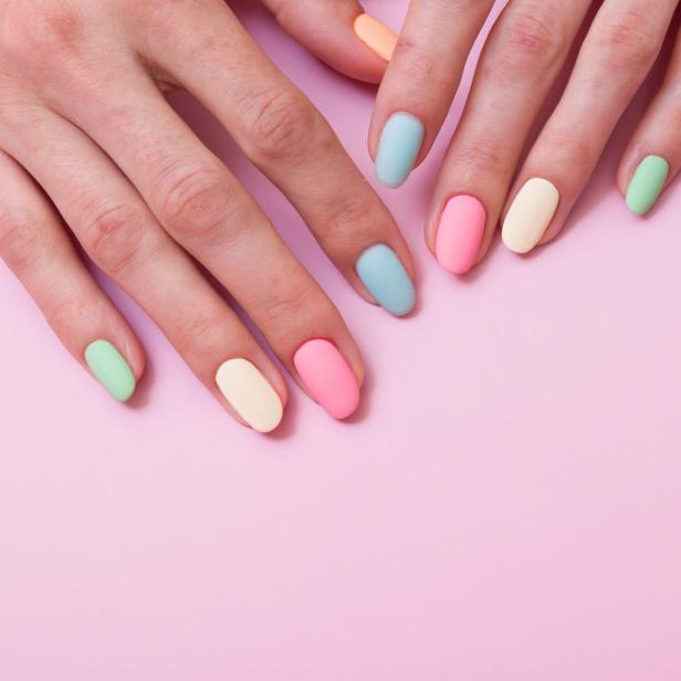 Hände mit pastellfarben lackierten Fingernägeln auf rosa Hintergrund.