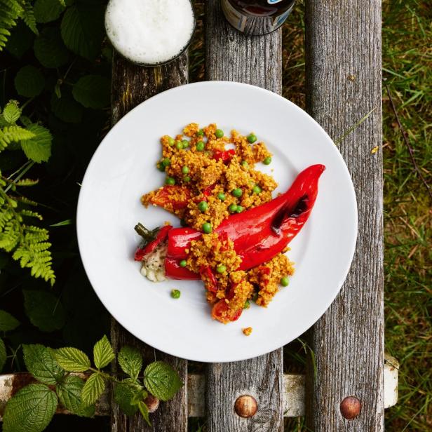 Ein Teller mit gefüllter Paprika und Couscous steht auf einer Holzbank neben einem Bier.