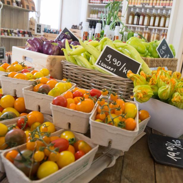 Verschiedene Gemüsesorten, darunter Tomaten, Paprika und Zucchiniblüten, werden in einem Laden zum Verkauf angeboten.