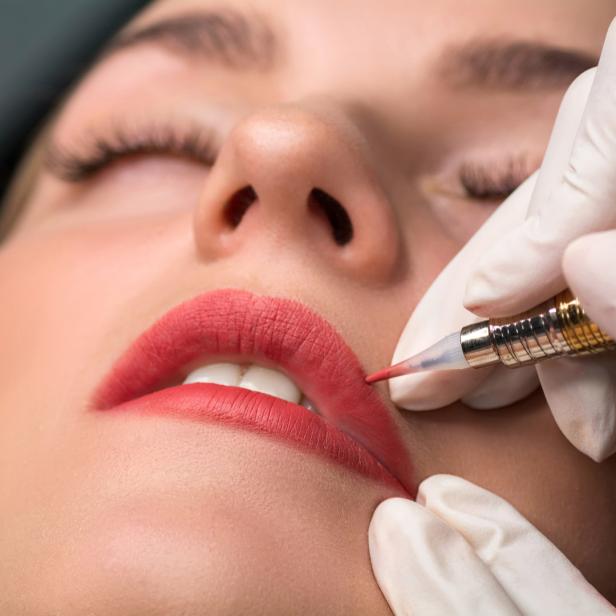 Eine Kosmetikerin pigmentiert die Lippen einer Frau mit einem Permanent-Make-up-Gerät.