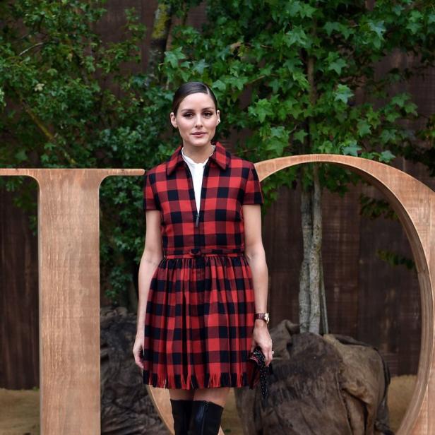 Olivia Palermo trägt ein rot-schwarzes Kleid und schwarze Stiefel vor einem „Dior“-Schriftzug.