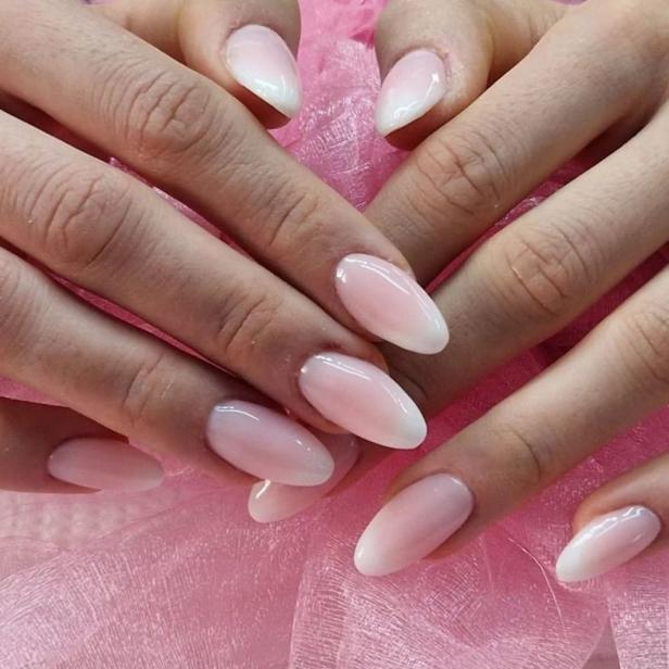 Nahaufnahme von Händen mit hellrosa-weißen Ombre-Nägeln auf einem rosa Tuch.