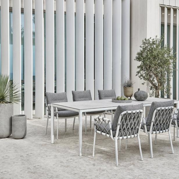Ein Esstisch mit Stühlen und grauen Polstern steht auf einer Terrasse.