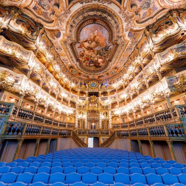 Innenansicht eines opulenten Theaters mit blau gepolsterten Sitzen und kunstvoller Deckenmalerei.