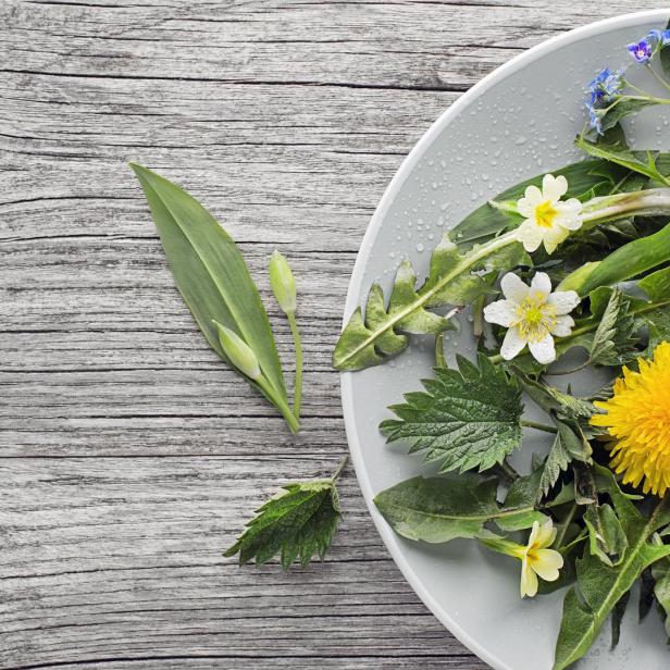 Ein Teller ist mit verschiedenen Wildblumen und grünen Blättern auf einem Holztisch dekoriert.