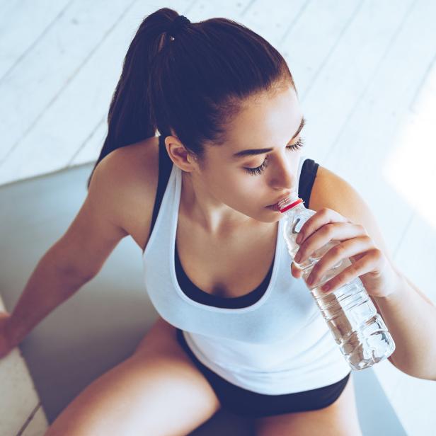 Eine Frau in Sportkleidung trinkt Wasser aus einer Plastikflasche.