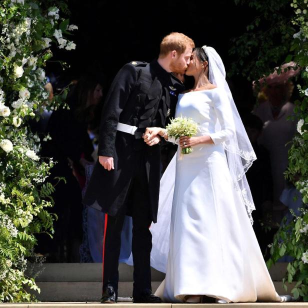 Prinz Harry und Meghan Markle küssen sich nach ihrer Hochzeit vor einem mit Blumen geschmückten Eingang.