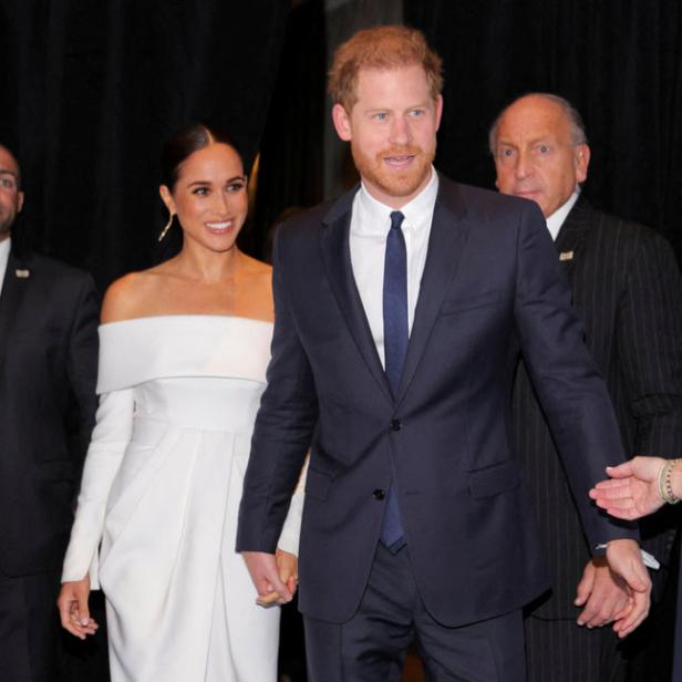 Prinz Harry und Meghan Markle Händchen haltend auf einem blauen Teppich.