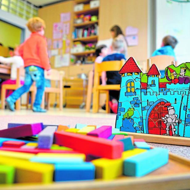 Kinder spielen in einer Kindertagesstätte mit einem Holzpuzzle und Bauklötzen.
