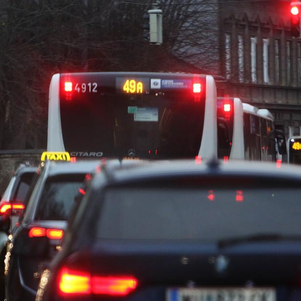 Mehrere Autos und Busse stehen bei Rot an einer Ampel in einer Stadtstraße.