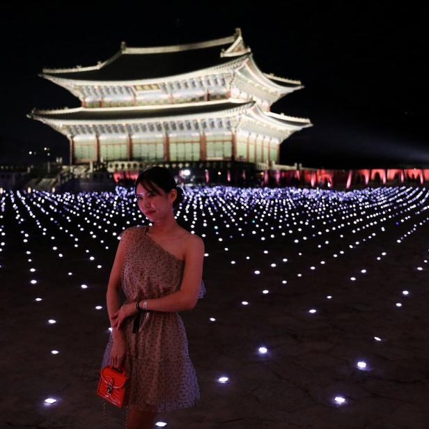 Eine Frau posiert vor dem Gyeongbokgung-Palast, der nachts beleuchtet ist.