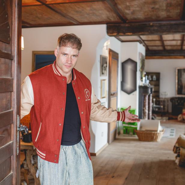 Ein Mann in Collegejacke und Pyjamahose steht in einer offenen Tür.