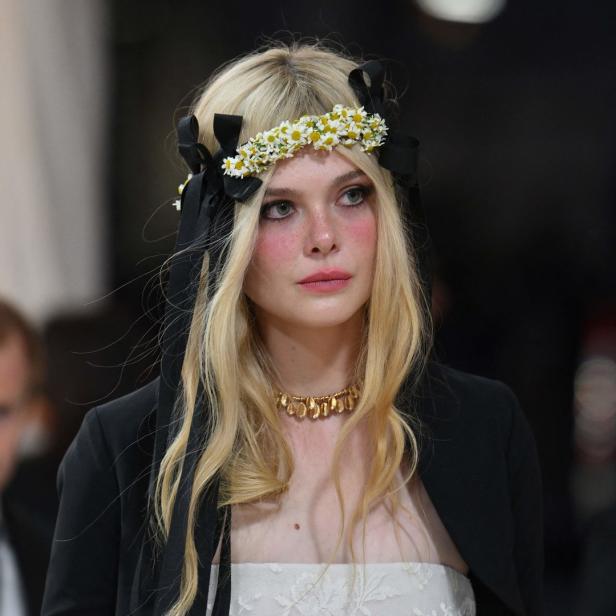 Elle Fanning mit blonden Haaren, Blumenkranz und schwarzem Blazer.