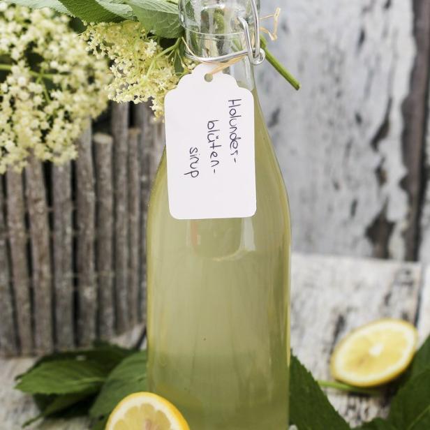 Eine Flasche Holunderblütensirup mit Zitronenscheiben und Minze auf einem Holztisch.