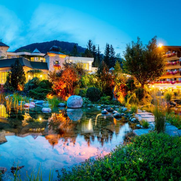 Ein Teich spiegelt die Lichter eines Hotels und der umliegenden Gärten wider.