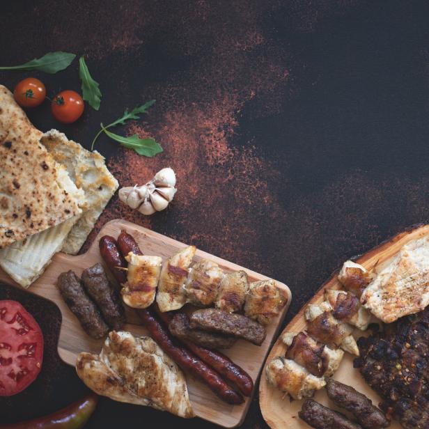 Cevapcici und gegrilltes Fleisch werden auf Holzbrettern mit Brot und Gemüse serviert.