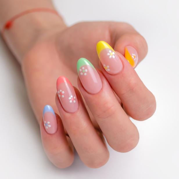 Eine Hand mit bunten, floral verzierten Nagelspitzen auf einem weißen Hintergrund.