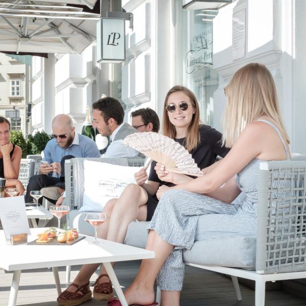 Eine Gruppe von Menschen sitzt in einem Straßencafé und genießt Getränke und Snacks.