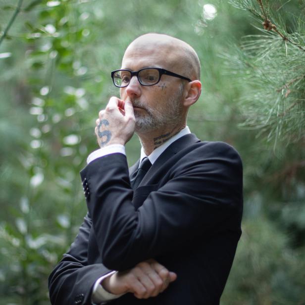 Moby in einem schwarzen Anzug steht nachdenklich im Grünen.