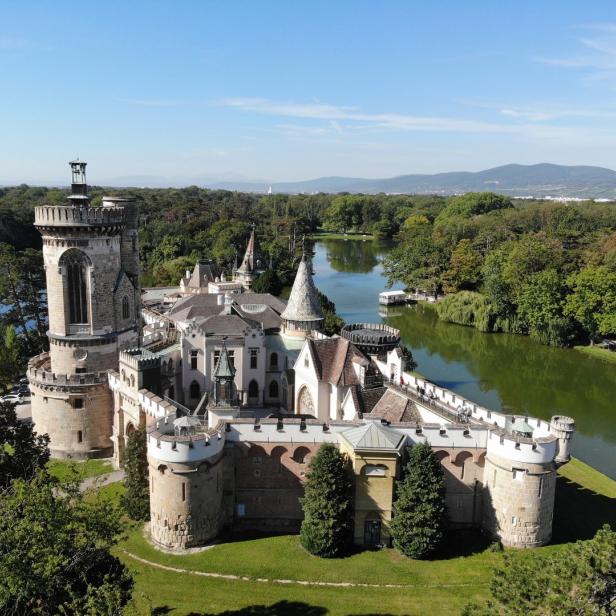 Luftaufnahme von Schloss Laxenburg, umgeben von einem See und grünen Bäumen.
