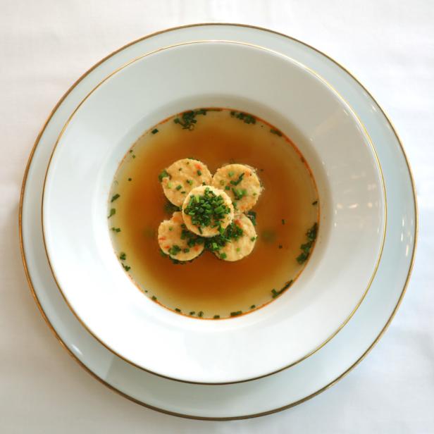Eine klare Suppe mit Kräutern und fünf Serviettenknödeln in einem weißen Teller.