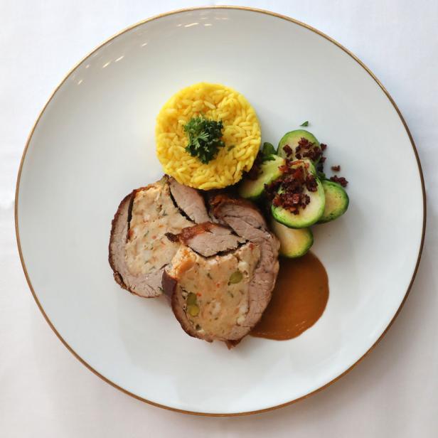 Ein Teller mit gefülltem Braten, gelbem Reis und Rosenkohl mit Speckwürfeln.