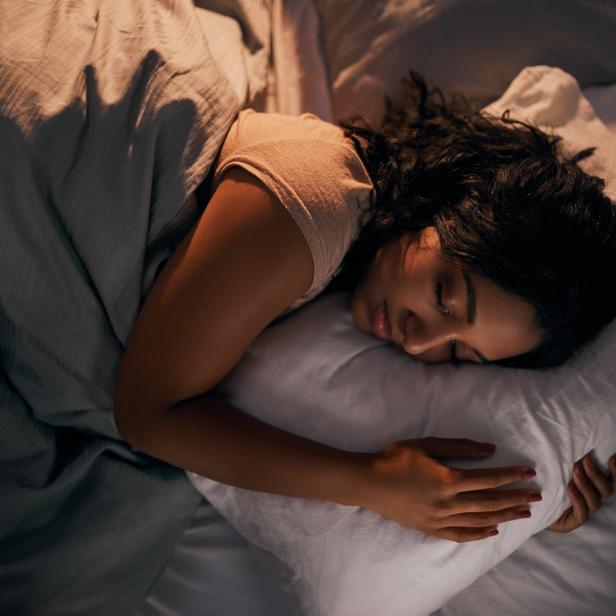 Eine Frau liegt mit geschlossenen Augen bei dämmrigem Licht im Bett.