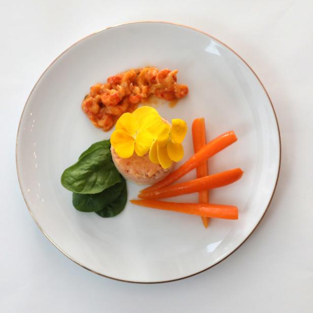 Ein Teller mit Krebsfleischsalat, garniert mit gelben Blüten, Babyspinat und Karotten.